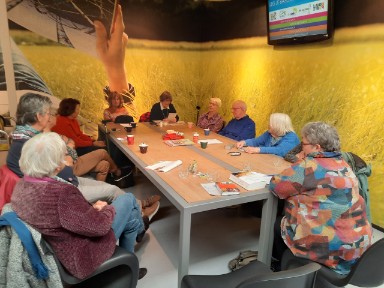 vier dames en een heer aan tafel in gesprek, elk met een boek