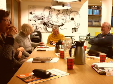 vier dames en een heer aan tafel in gesprek, elk met een boek