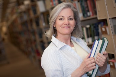 vrouw met stapel boeken voor boekenkast